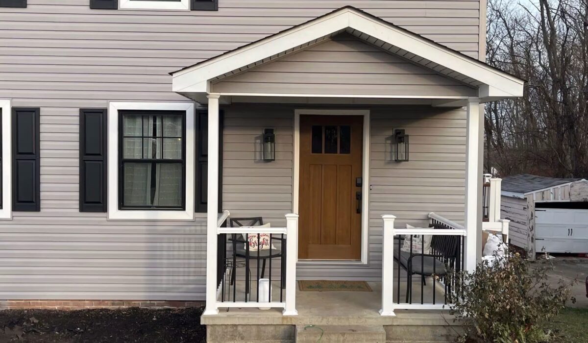 Front porch of a residential home featuring gray siding, black shutters, and a wooden door, illustrating modern exterior design for Pittsburgh homeowners.