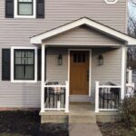 Front entrance of a residential home with a wooden door, white railings, and black shutters, emphasizing exterior design and potential roofing and ventilation improvements for Pittsburgh homeowners.