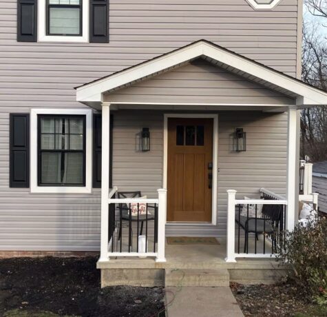 Home exterior featuring a modern porch with a wooden front door, white railings, and black shutters, showcasing siding suitable for Pittsburgh's weather resilience.