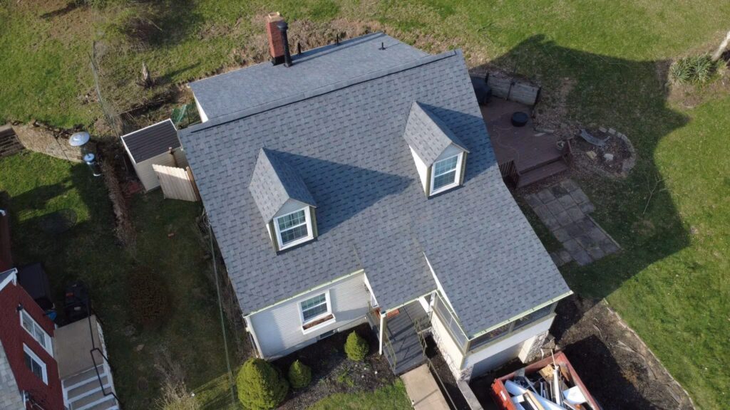 Aerial view of a house with a newly installed gray shingle roof, showcasing well-maintained landscaping and outdoor space, relevant to roof replacement services in Pittsburgh.