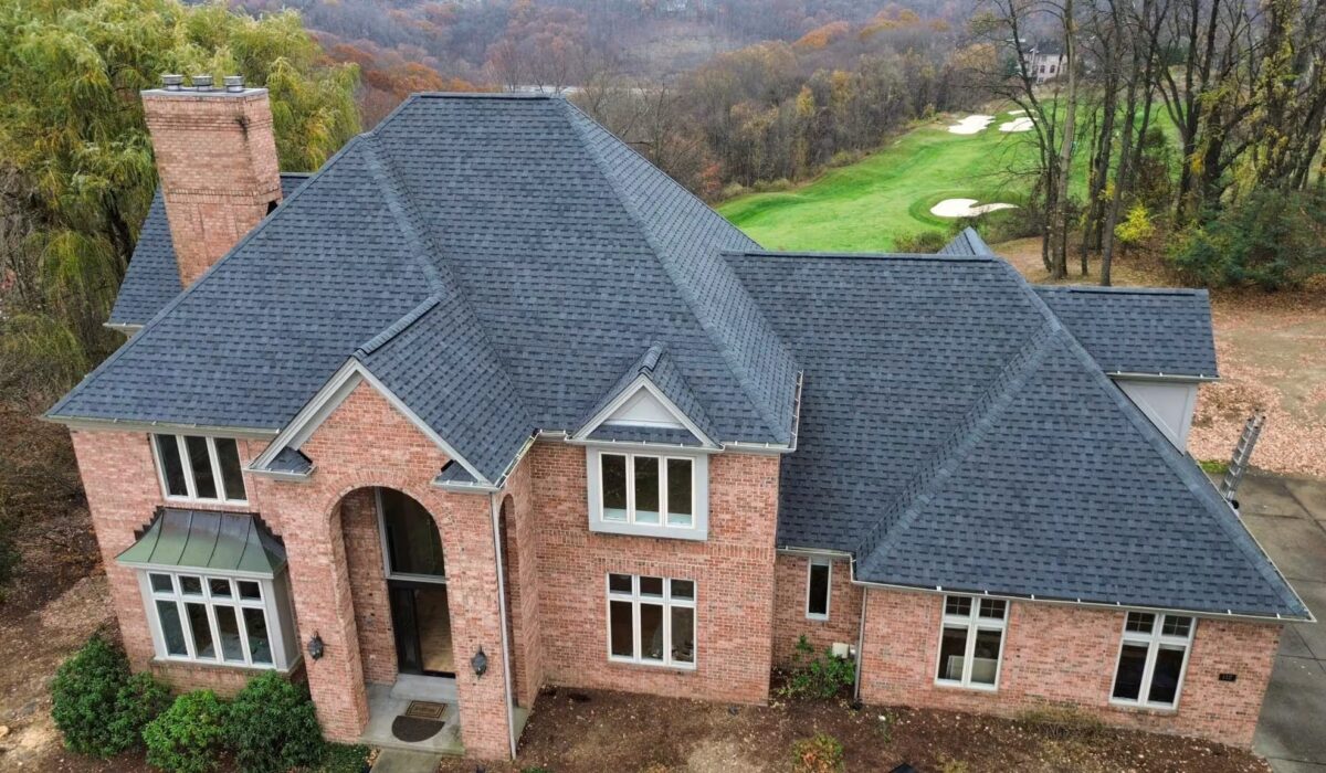 Aerial view of a residential home featuring a dark shingle roof, brick exterior, surrounded by greenery and a golf course in the background, illustrating roofing options discussed in 2025.