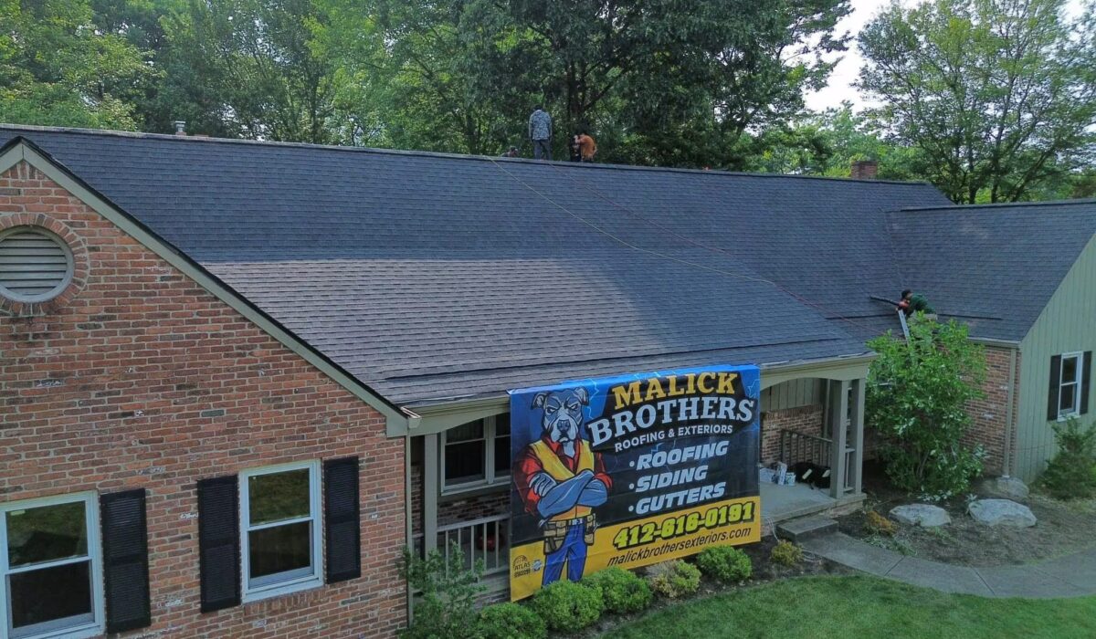 Roofing installation by Malick Brothers Exteriors with workers on a shingled roof, featuring a promotional banner for roofing, siding, and gutters.