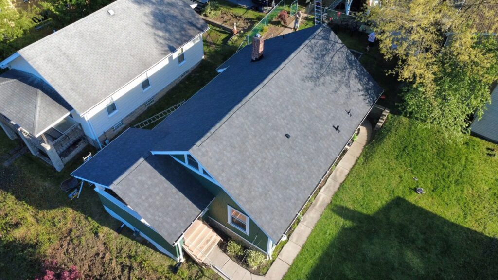Aerial view of a residential home with a newly installed asphalt shingle roof, surrounded by green lawn and neighboring houses, illustrating durable roofing solutions suitable for Pittsburgh's climate.