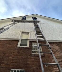 Workers on a ladder performing exterior maintenance on a residential building, emphasizing quality craftsmanship in roofing solutions.