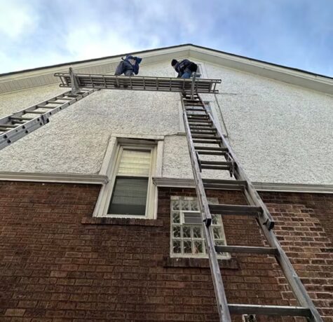 Workers on a ladder performing exterior maintenance on a building, highlighting commercial roofing services by Malick Brothers Exteriors.