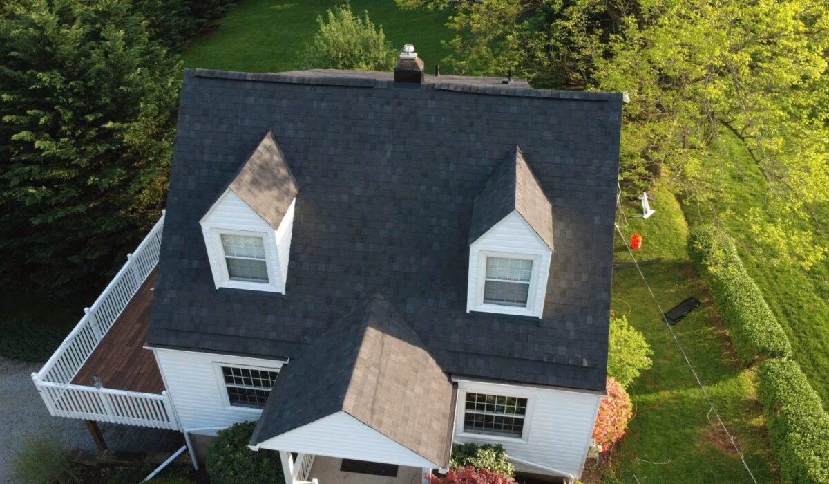 Aerial view of a house with a dark asphalt shingle roof, highlighting the roof's durability and design, surrounded by green landscaping, relevant to asphalt roofing choices in Pennsylvania for 2025.