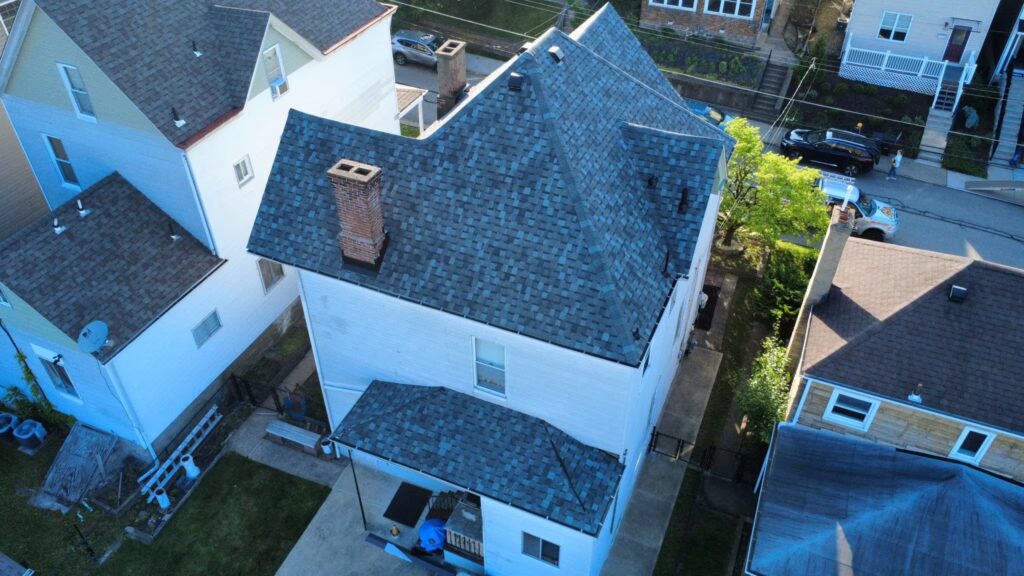 Aerial view of a residential building with asphalt shingle roofing, highlighting multiple roof angles and a chimney, relevant to discussions on roof age and insurance coverage.