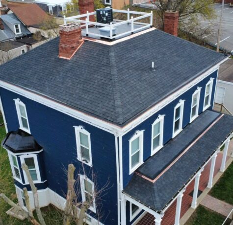 Aerial view of a blue house with a newly installed dark shingle roof, showcasing roofing quality and exterior design, relevant to home improvement and maintenance in Pittsburgh.