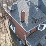 Aerial view of a residential roof featuring Atlas Pinnacle Pristine shingles, highlighting the structure's multiple slopes and chimney, relevant for homeowners in Pittsburgh considering roofing contractors.