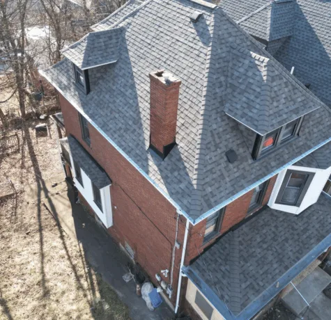 Roofing installation on a brick house in Pittsburgh, showcasing quality craftsmanship with dark shingles and chimney, emphasizing exterior maintenance and services by Malick Brothers Exteriors.