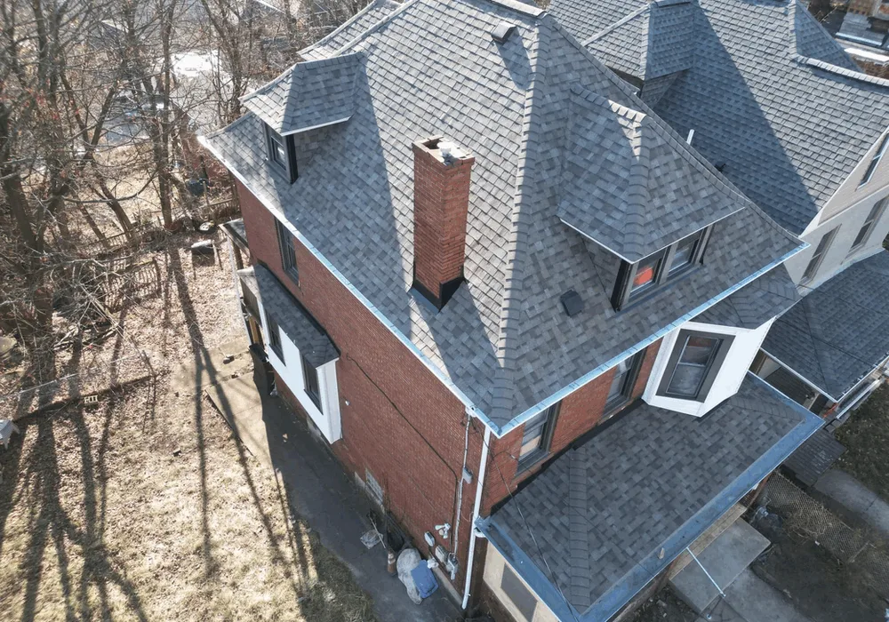 Aerial view of a residential roof in Pittsburgh, showcasing a well-maintained shingle roof with multiple peaks and a chimney, emphasizing the importance of spring roof inspections after winter weather.
