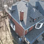 Aerial view of a residential roof featuring dark shingles, multiple peaks, and a brick chimney, illustrating roofing quality and design relevant to Pittsburgh roofing services.