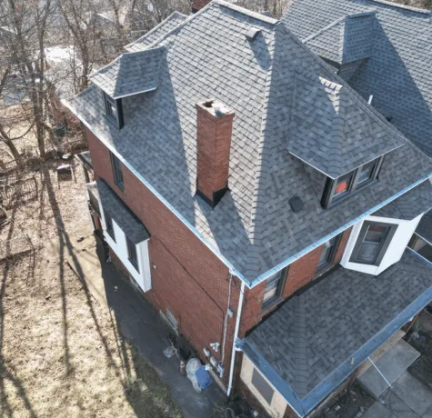 Aerial view of a residential roof featuring gray shingles, a chimney, and adjacent brick walls, showcasing quality roofing craftsmanship by Malick Brothers Exteriors in Pittsburgh.