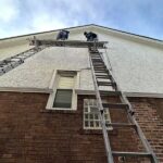 Workers on a ladder performing maintenance on a residential roof, emphasizing proactive care for aging roofs.