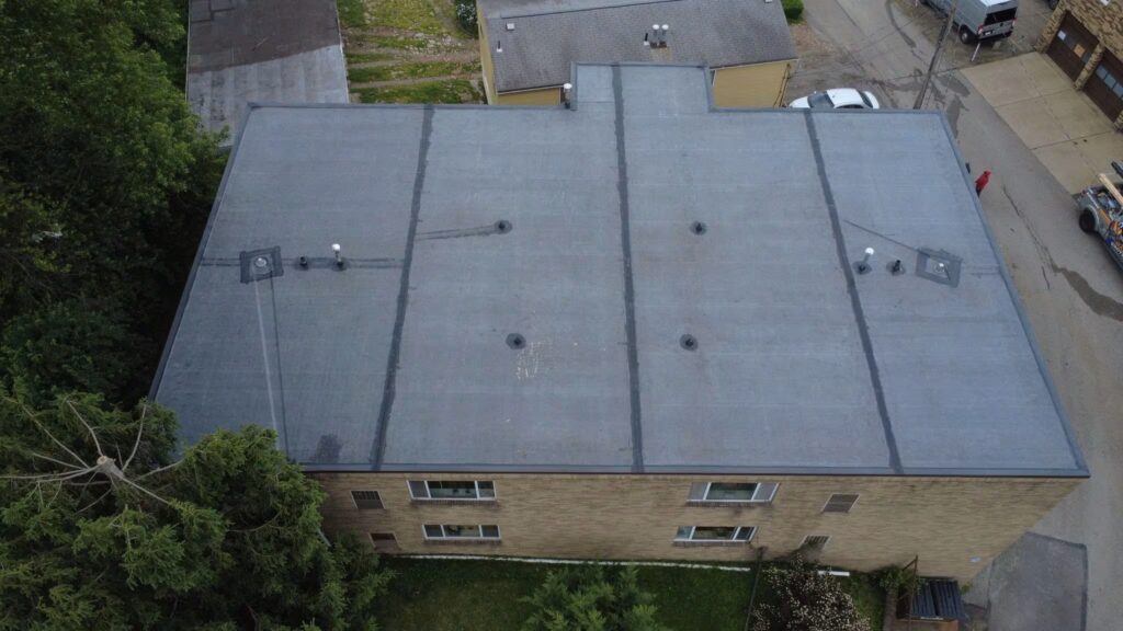 Flat roof of a Pittsburgh rowhome featuring ventilation systems, surrounded by greenery and adjacent buildings, illustrating the importance of proper ventilation for moisture and heat management.