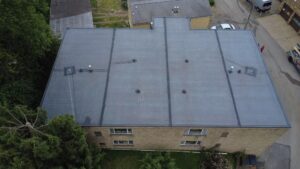 Aerial view of a commercial flat roof with visible drainage vents and surrounding greenery, illustrating potential areas for ponding water and flashing failures relevant to roof maintenance in Pittsburgh.