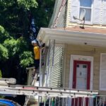Worker on ladder inspecting soffit and fascia on residential building, highlighting roofing maintenance in Pittsburgh.