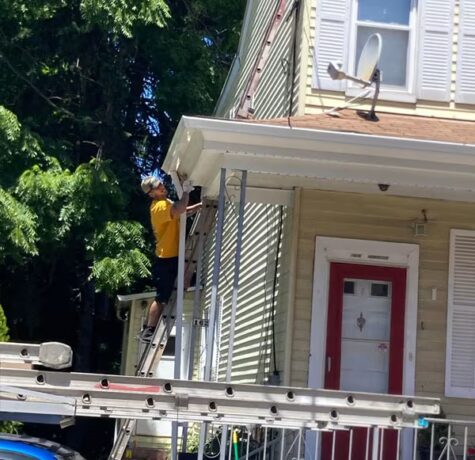 Worker on ladder performing soffit and fascia repair on historic home in Pittsburgh, showcasing roofing maintenance techniques.