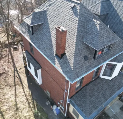 Aerial view of a residential home in Pittsburgh featuring a newly installed asphalt shingle roof, highlighting quality craftsmanship by Malick Brothers Exteriors, with a chimney and surrounding trees visible.