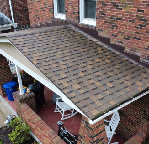 Roofing shingles in a residential setting, showcasing a well-maintained porch roof with a mix of brown and tan shingles, surrounded by brick walls and outdoor furniture, relevant to roofing solutions in Pittsburgh.