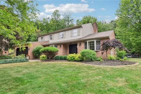 Two-story brick home with well-maintained landscaping, featuring a manicured lawn and shrubs, situated in a residential area, relevant to Malick Brothers Exteriors' focus on roofing and exterior solutions for homeowners in Pittsburgh.