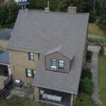 Residential roofing installation on a brick house in Pittsburgh, showcasing a well-maintained gray shingle roof and surrounding greenery.