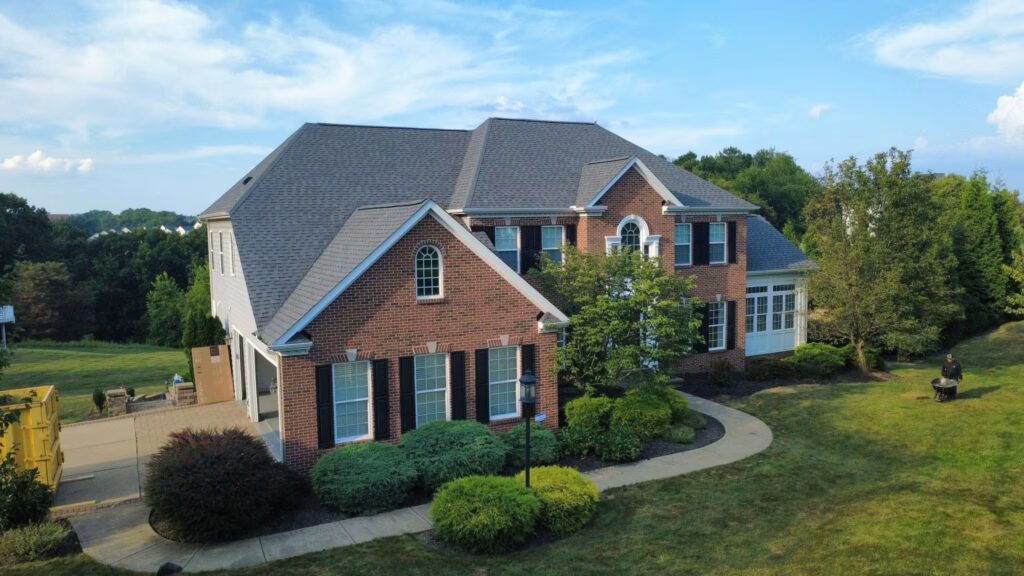 Residential home in Pittsburgh featuring a newly installed shingle roof, surrounded by landscaped greenery and a clear blue sky, illustrating the benefits of professional roofing services.