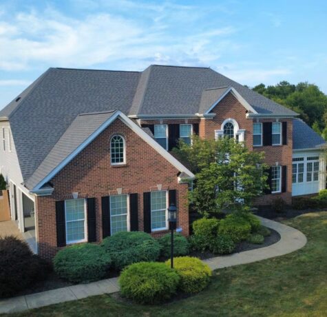 Elegant brick home with a new roof, surrounded by lush landscaping and a curved walkway, showcasing quality exterior solutions by Malick Brothers Exteriors in Pittsburgh.