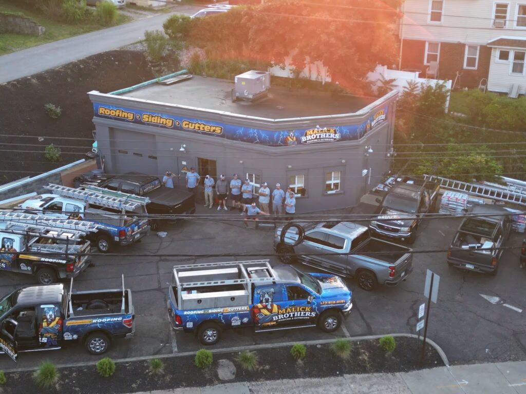 Malick Brothers Exteriors building with branding, crew of contractors, and service vehicles parked outside, showcasing commercial roofing and exterior solutions.