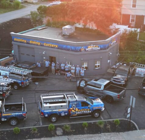 Malick Brothers Exteriors team outside their roofing and siding business location in Pittsburgh, showcasing trucks with branding and services offered.