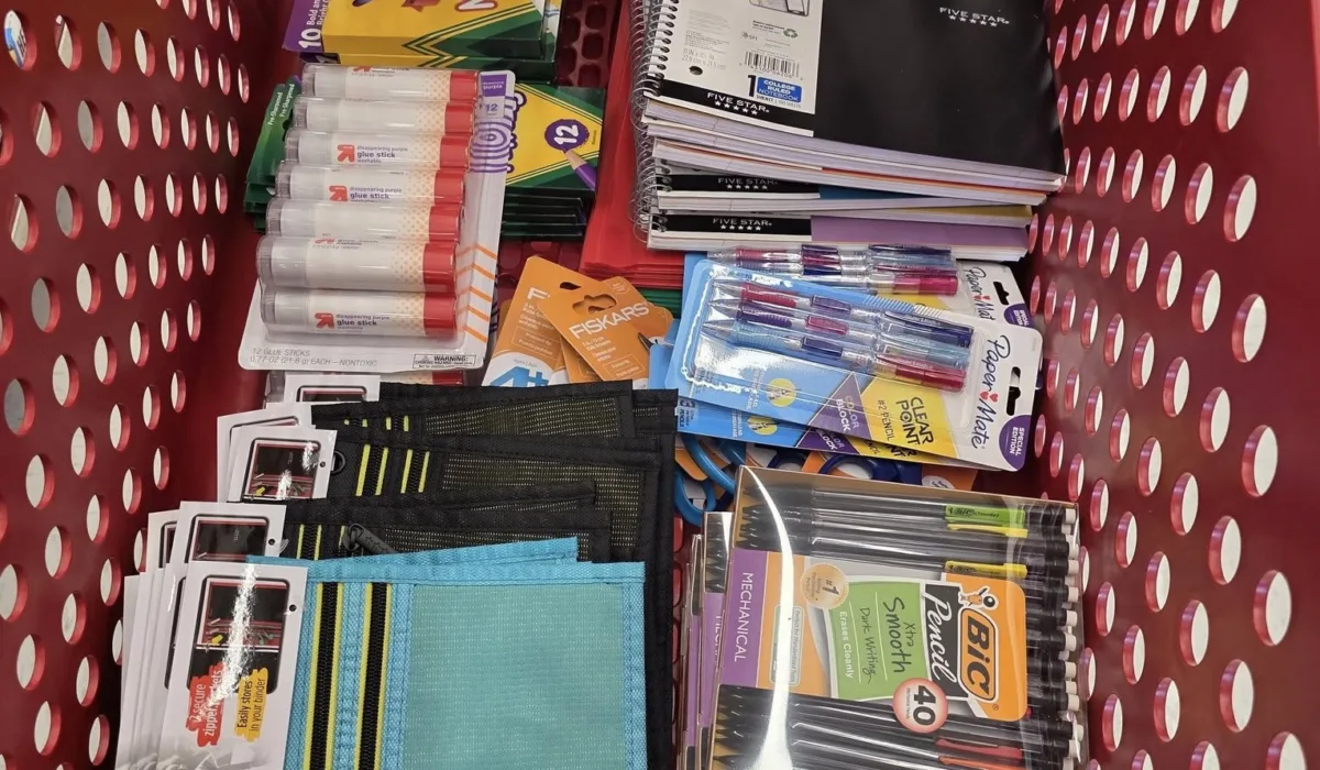 Assorted school supplies including glue sticks, notebooks, pens, and pencil cases, organized in a red shopping cart, supporting Malick Brothers Exteriors' community outreach school supply drive.