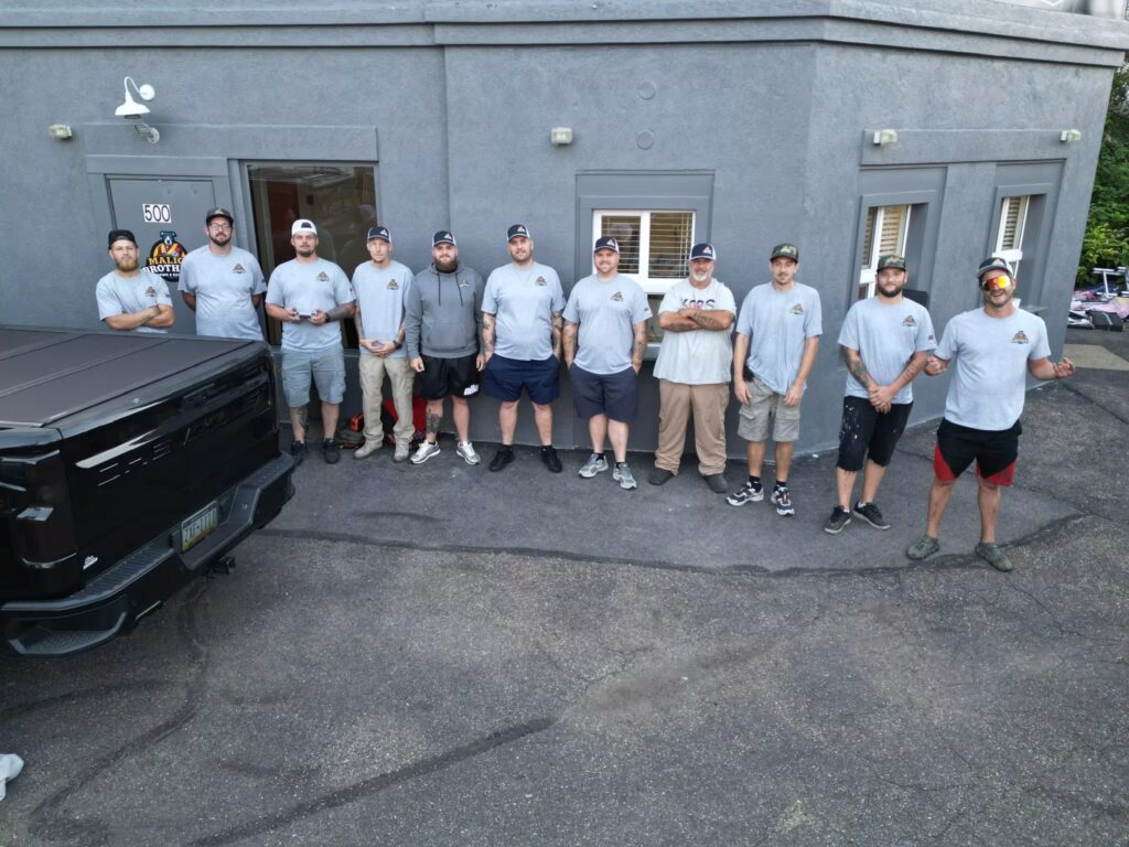 Group of Malick Brothers Exteriors team members in gray shirts standing outside their office, showcasing teamwork and professionalism in roofing and exterior solutions.