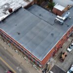 Aerial view of a commercial flat roof, showcasing its gray surface and surrounding brick building, relevant to discussions on commercial roofing lifespan and maintenance.