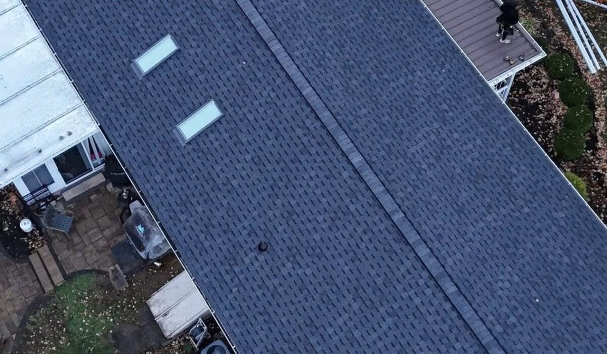 Aerial view of a dark shingle roof with skylights, adjacent to a lighter roof, showcasing roofing materials relevant to commercial and residential buildings.