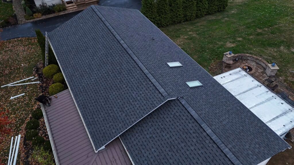 Aerial view of a residential roof featuring dark shingles, skylights, and surrounding landscaped yard, illustrating roofing solutions relevant to commercial and industrial needs.