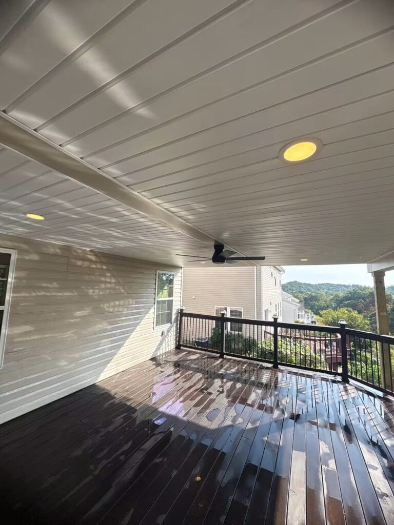 Covered outdoor deck with wet wooden flooring, ceiling fan, and overhead lighting, showcasing quality craftsmanship and design relevant to roofing and exterior solutions.