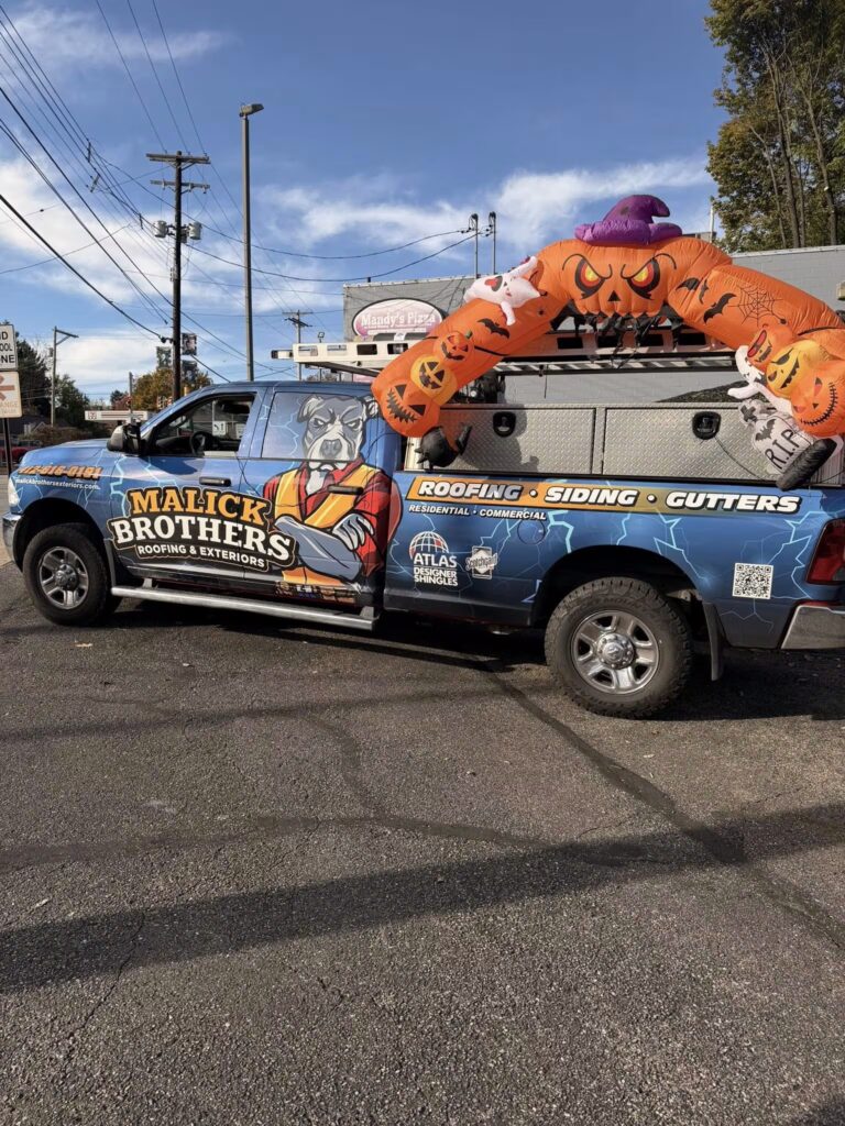 Malick Brothers Exteriors branded truck with Halloween decorations, featuring services for roofing, siding, and gutters, parked in a commercial area.