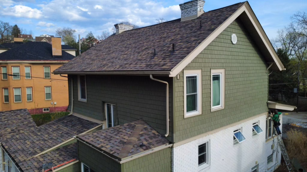 Roof of a green residential building with shingles, showcasing proper drainage systems and maintenance work in Pittsburgh's climate.