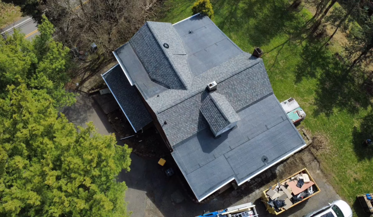 Aerial view of a commercial building with a newly installed dark shingle roof, surrounded by trees and construction equipment, relevant to Pittsburgh roof restoration and replacement discussions.
