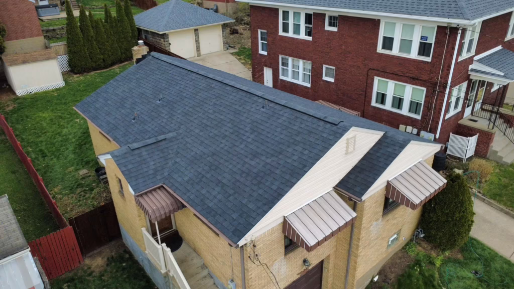 Aerial view of a residential building in Pittsburgh with a newly installed dark shingle roof, showcasing proper roofing techniques for local climate challenges.