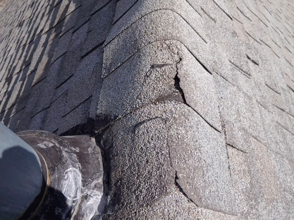 Close-up of cracked and deteriorated ridge cap shingles on an asphalt roof