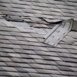 Missing and torn asphalt shingles exposing the roof underlayment after wind damage