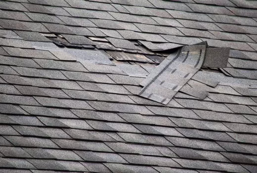 Missing and torn asphalt shingles exposing the roof underlayment after wind damage