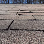 Lifted and buckled asphalt roof shingles showing signs of roof damage