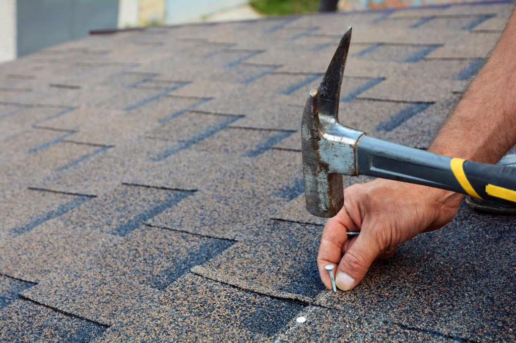 Roofer repairing asphalt shingles with a hammer and roofing nails