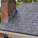 Brick chimney with copper step flashing and counterflashing on a slate roof surrounded by trees in Western Pennsylvania