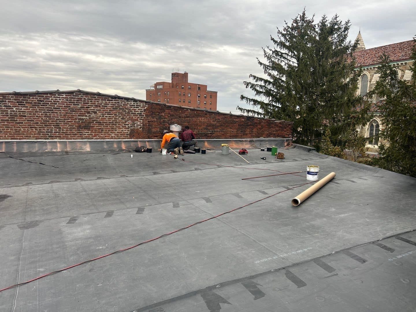 Malick Brothers Exteriors crew working on a large flat commercial roof in Pittsburgh under cloudy skies
